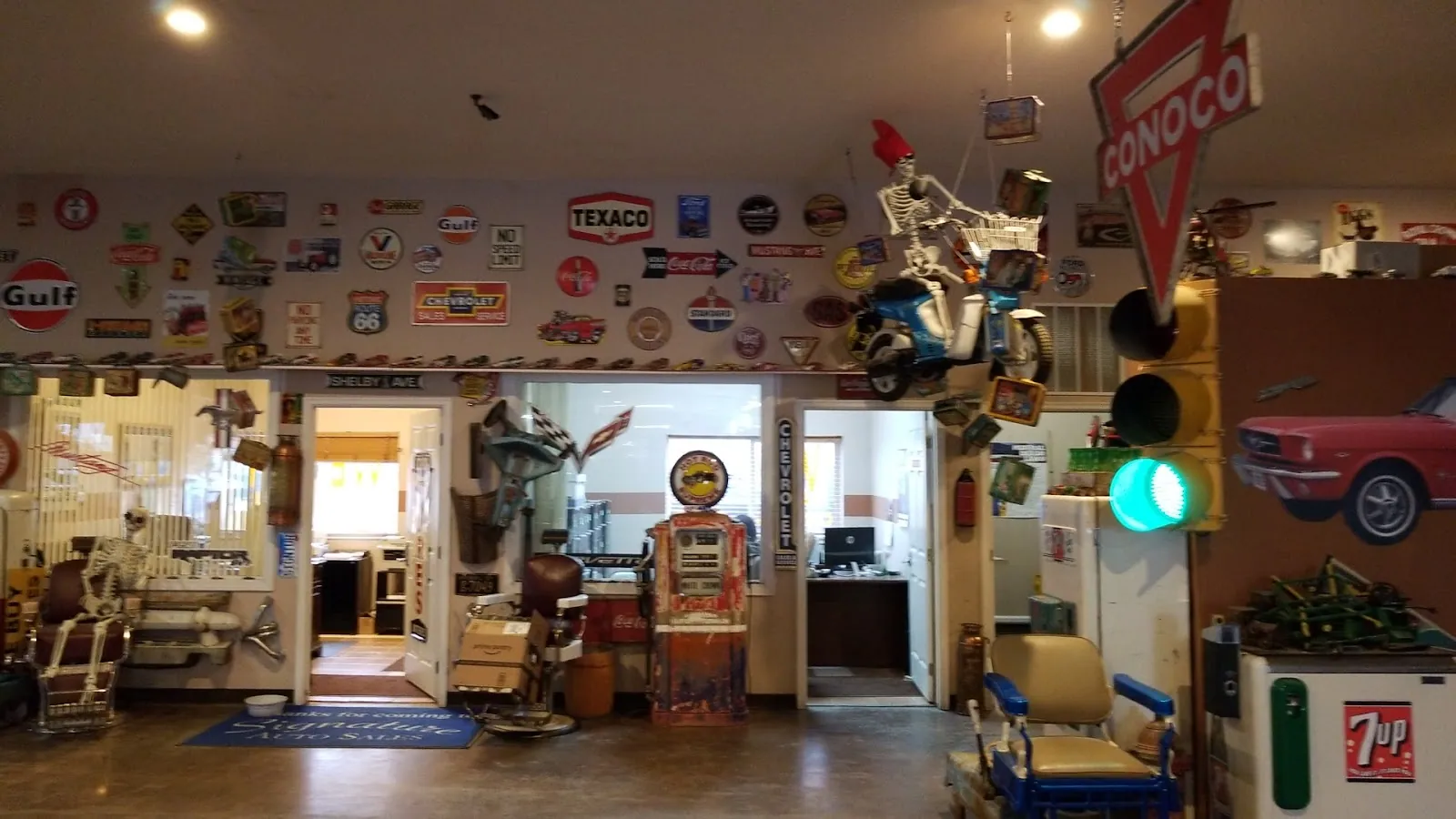 A showroom wall covered in Gulf, Texaco and Conoco signs, with a traffic light showing green beside an open doorway.