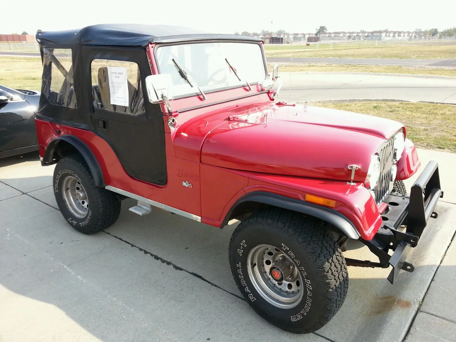 A red Jeep CJ-5 with a black soft top, parked on the concrete.